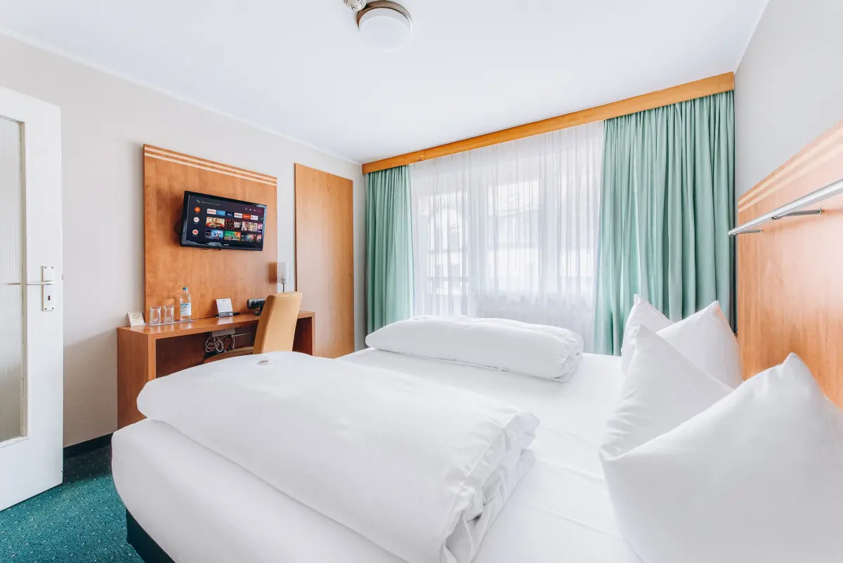 Doppelzimmer mit mintgrünen Vorhängen und Holzmöbeln