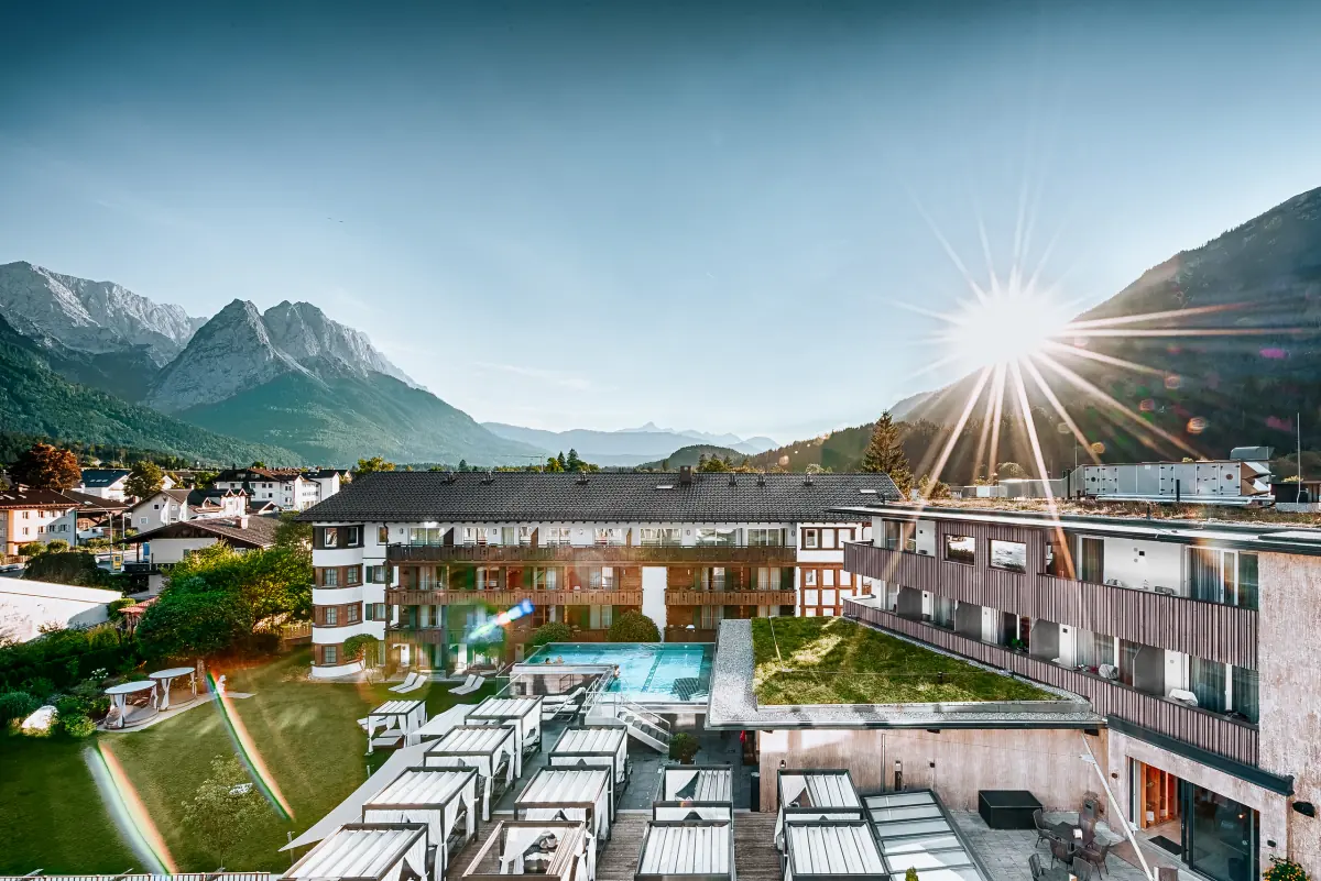 Hotelanlage von oben mit Pool und Garten vor dem Bergpanorama