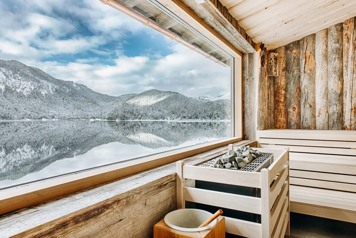 Sauna mit Panoramafenster auf verschneite Berge und einen See