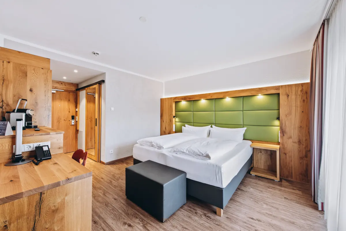 Doppelzimmer mit grün gepolstertem Kopfteil und Holzmöbeln