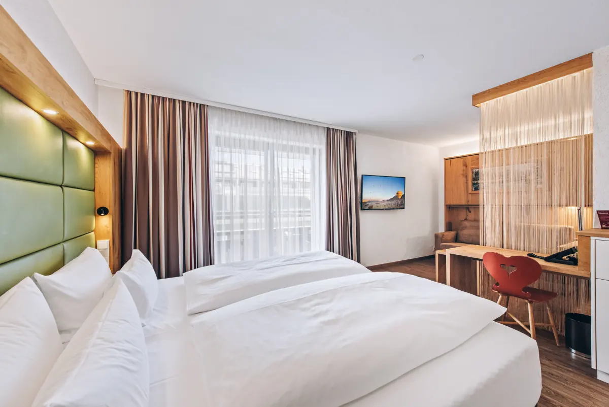 Helles Doppelzimmer mit grünem Kopfteil und Raumteiler